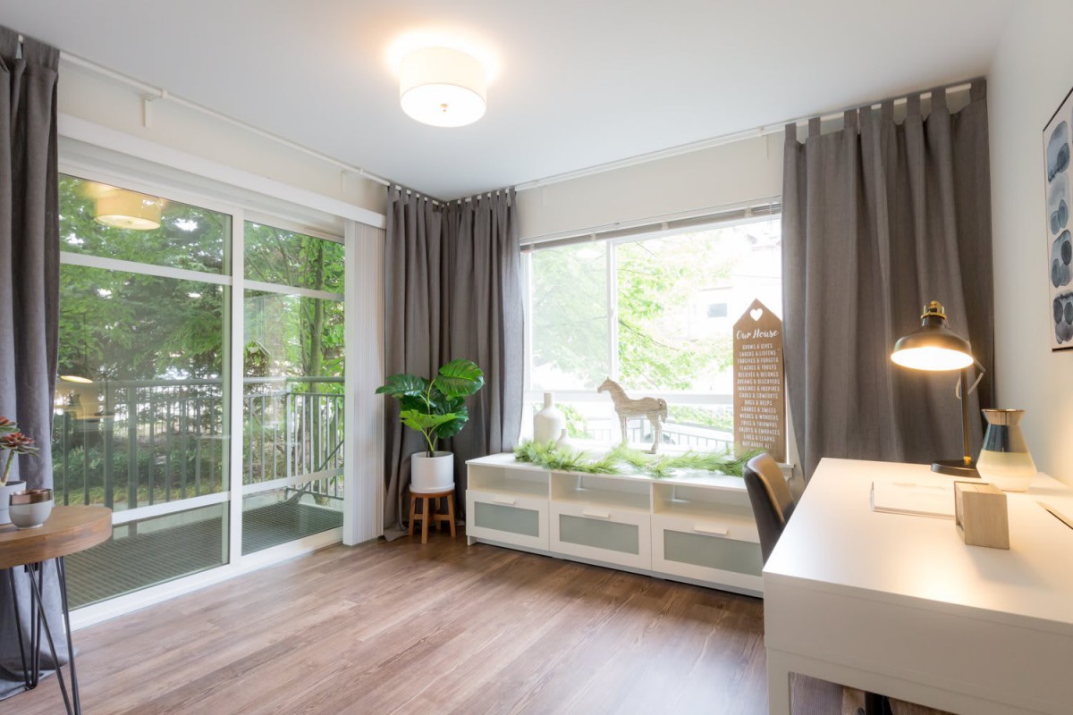 A bright and modern home office with natural light, featuring a desk, wooden flooring, plants, and decorative elements.