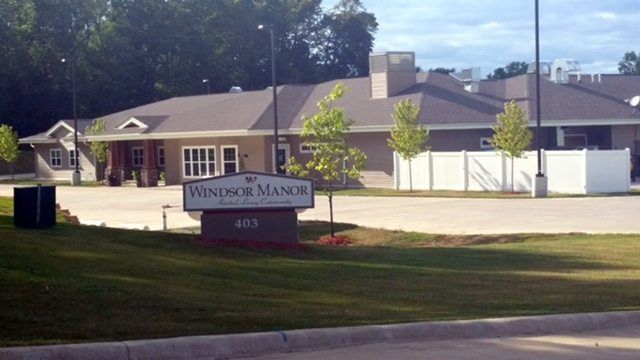 A view of a building with a sign reading 'Windsor Manor' and a well-maintained lawn in the foreground.