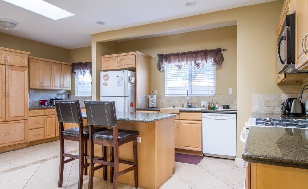 A modern kitchen with wooden cabinetry, featuring a central island with bar stools and various appliances.