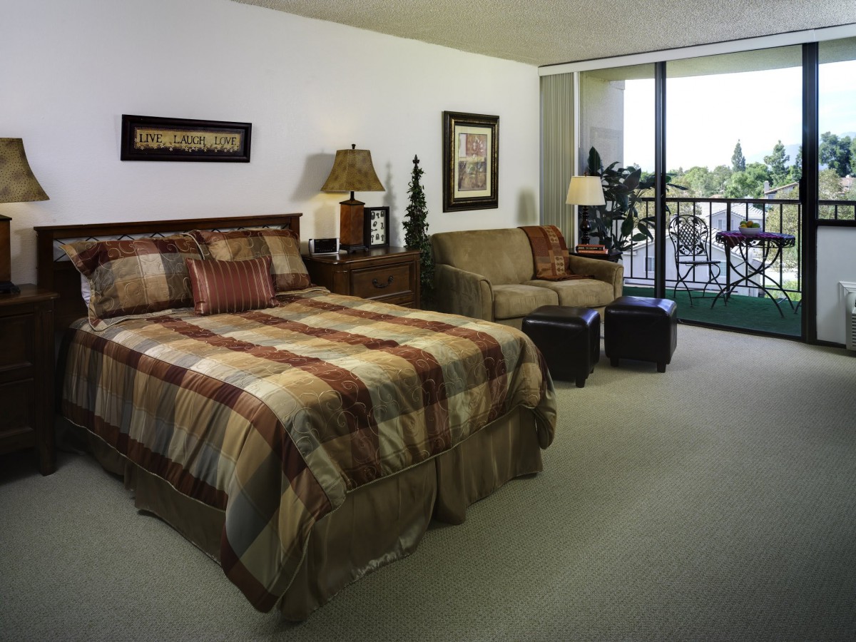 A cozy bedroom with a bed and sofa, featuring warm decor and a large window.