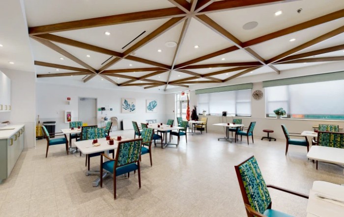 A modern dining area with stylish chairs and tables, accented by wooden ceiling beams and ample natural lighting.