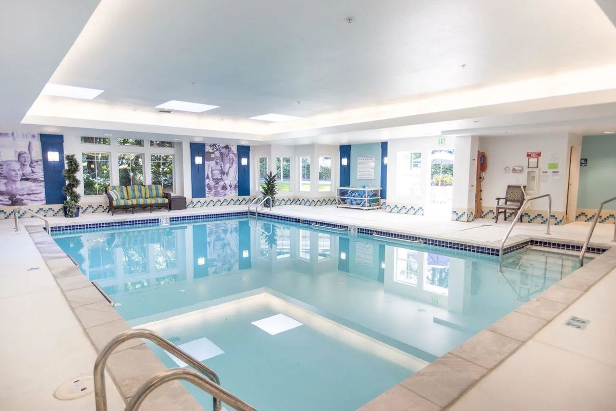 A well-lit indoor swimming pool area with modern decor and seating.