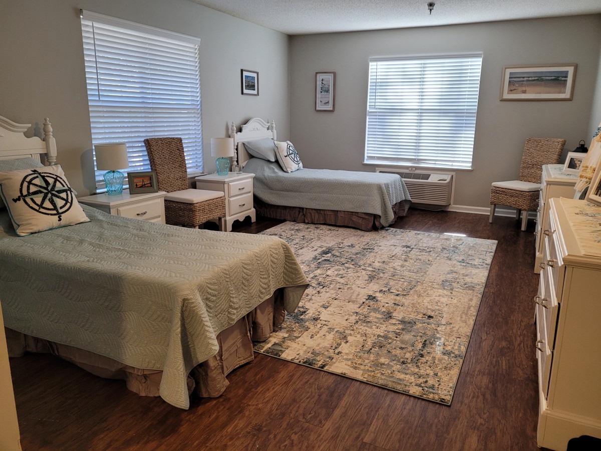 A cozy bedroom with two beds, featuring a decorative rug and ample natural light.