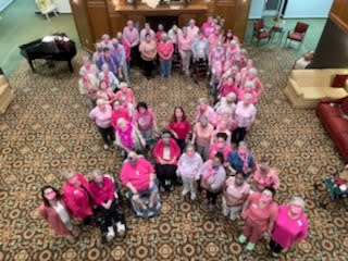 A group of people wearing pink arranged in the shape of a ribbon to support breast cancer awareness.
