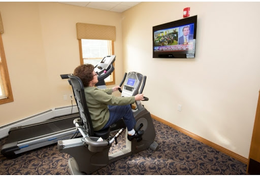 A person exercising on a recumbent bike in a fitness room while watching television.