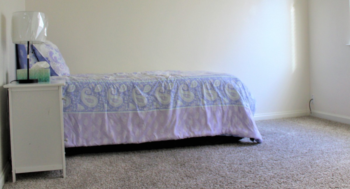 A minimalist bedroom with a bed covered by a patterned blanket on a carpeted floor.