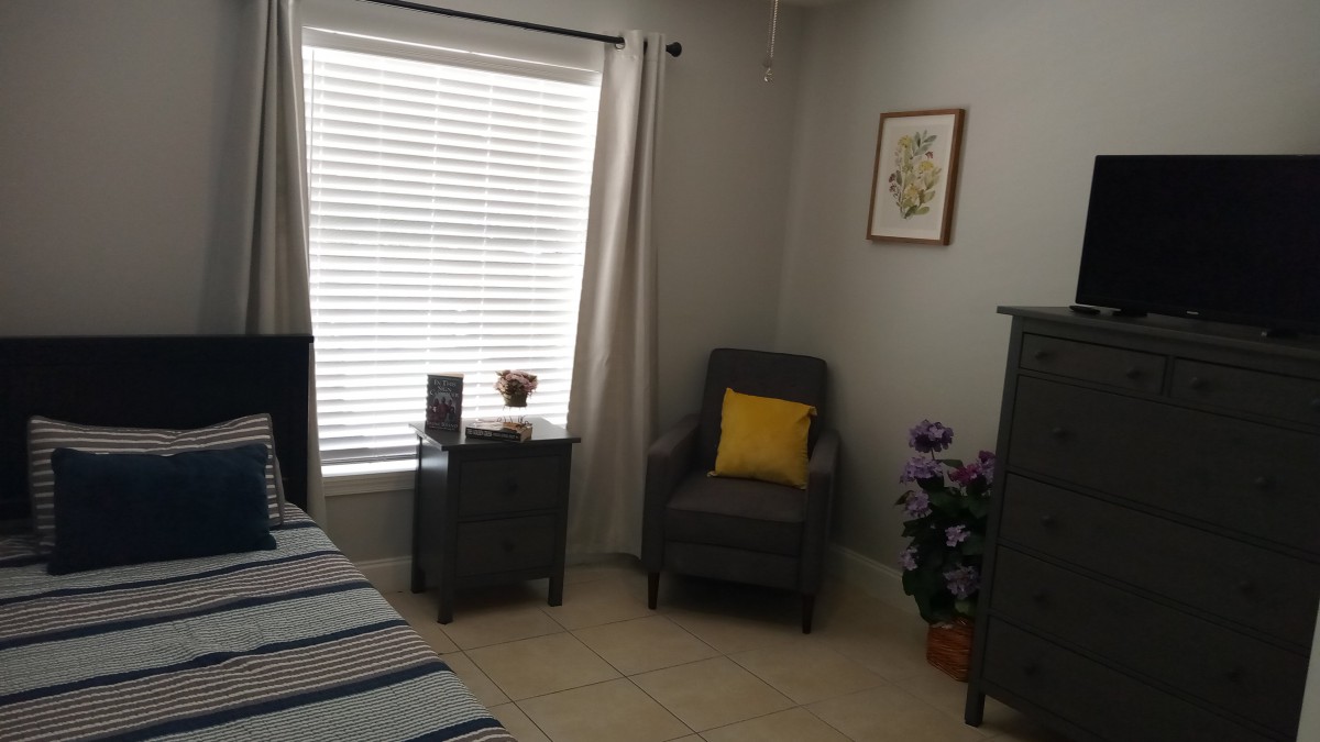 A cozy bedroom corner with a chair, pillow, and a small table by the window.