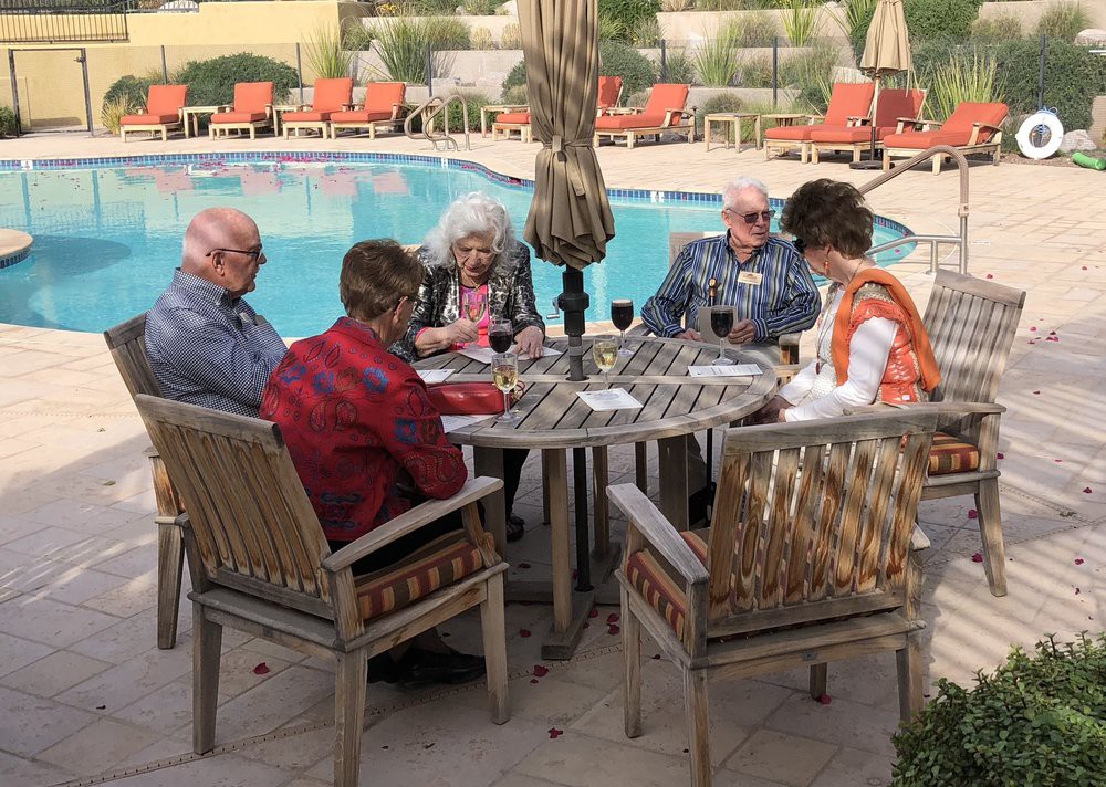 A group of seniors sitting around a table by the pool, socializing and enjoying the outdoors.