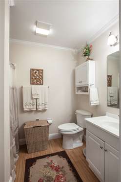 A small, neatly organized bathroom with a toilet, sink, and mirror.