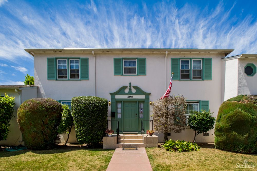 A two-story residential building with green shutters and a front entryway, displaying an American flag.