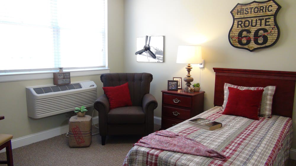 A cozy bedroom with a neatly made bed, comfortable chair, and a lamp on the nightstand.
