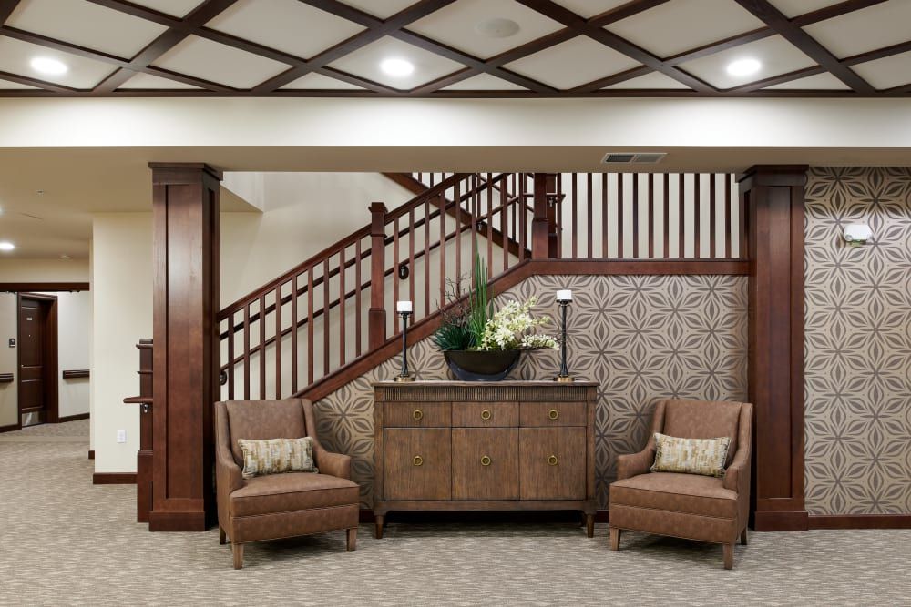 A traditionally designed living space featuring wooden stairs, armchairs, and a central cabinet.