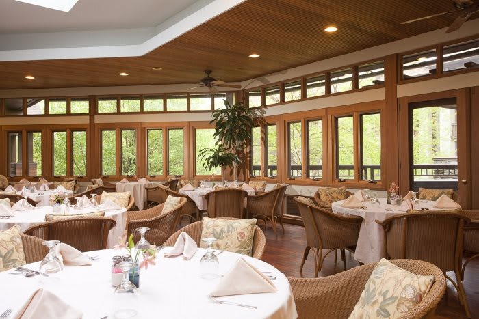 A cozy dining area with tables and wicker chairs, surrounded by large windows.