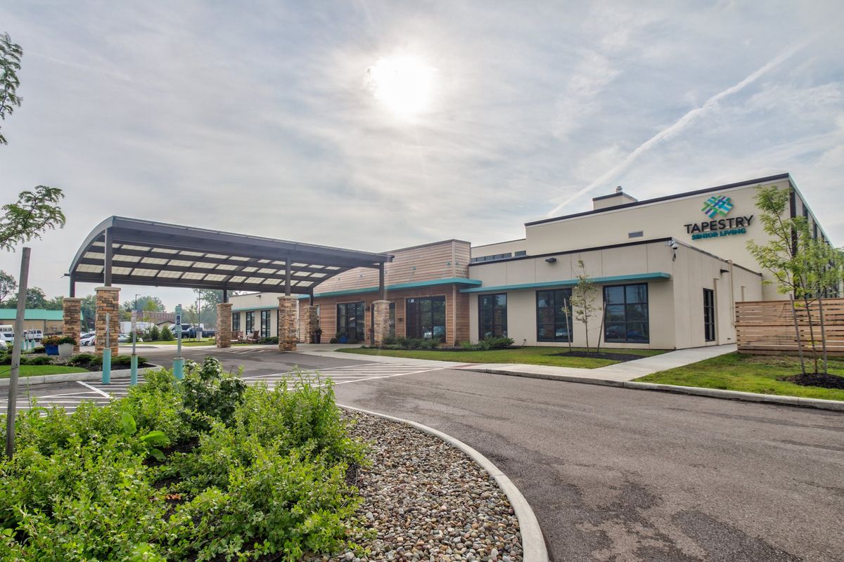 Modern building with a covered driveway and landscaped surroundings on a sunny day.