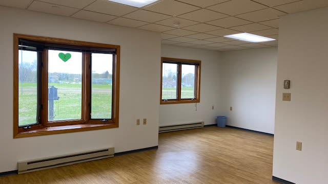An empty room with wooden floors and large windows allowing natural light in.