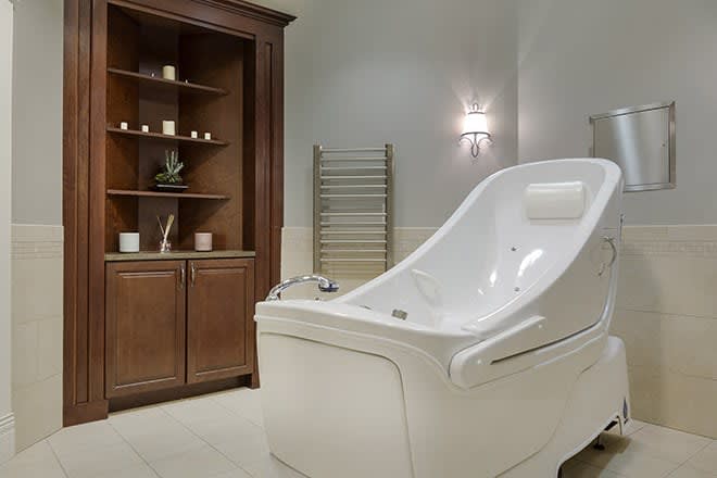 A luxurious spa bathroom featuring an elegant white bathtub with a wooden cabinet for storage.