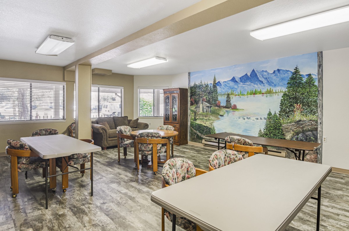 A spacious room with tables, chairs, and couches, featuring a scenic mural on the wall.