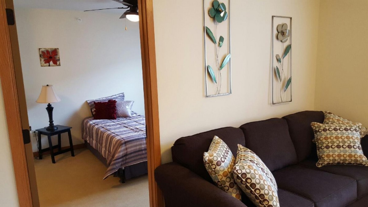 A cozy living room with a view into the bedroom, decorated with floral wall art and accent pillows.