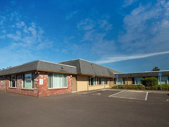 A single-story office building with an adjacent parking lot under a clear blue sky.