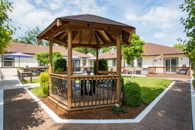A wooden gazebo surrounded by a landscaped garden with vibrant greenery.