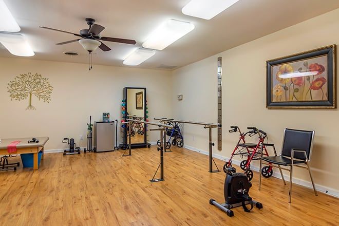 A physical therapy room equipped with parallel bars, a walker, and other exercise equipment.