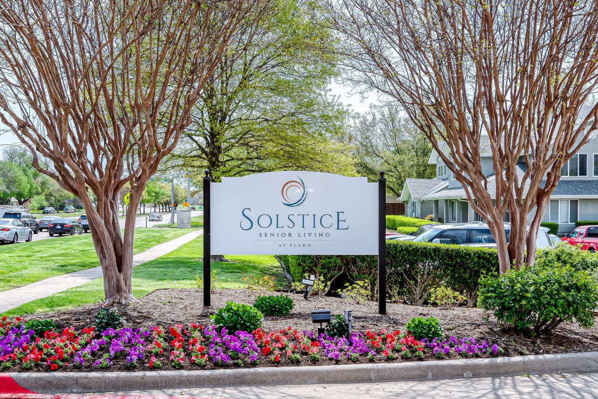 A landscaped entrance sign surrounded by colorful flowers and trees.