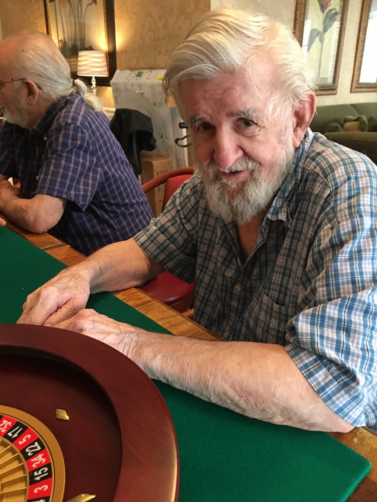 An elderly man sitting at a roulette table, ready to play.