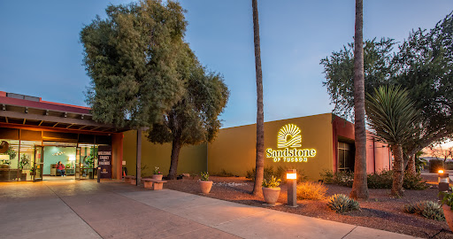 A modern building illuminated in the evening, featuring inviting landscaping and a prominent sign.