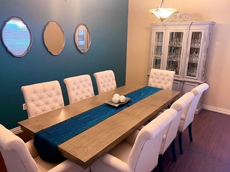 A modern dining room with a sleek wooden table, white upholstered chairs, and a blue accent wall adorned with mirrors.