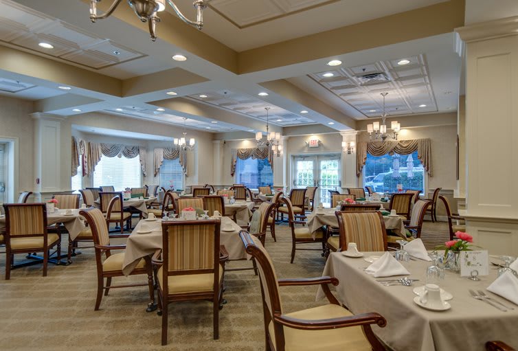 An elegant dining room with neatly arranged tables and chairs, featuring chandeliers and decorative elements.