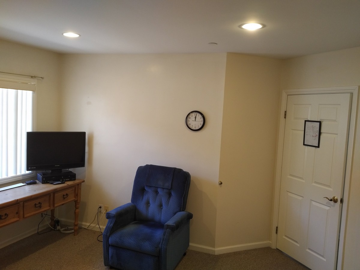 A cozy living room with a blue armchair, television, and wall clock.