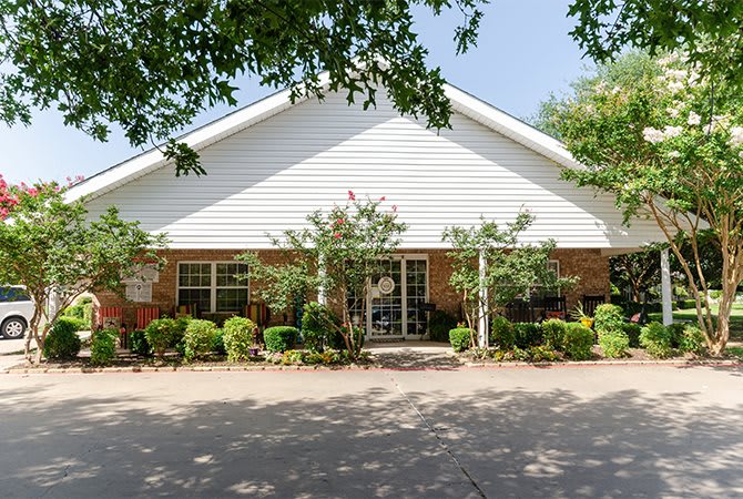 A well-maintained residential building with a front yard featuring trees and shrubs under a sunny sky.