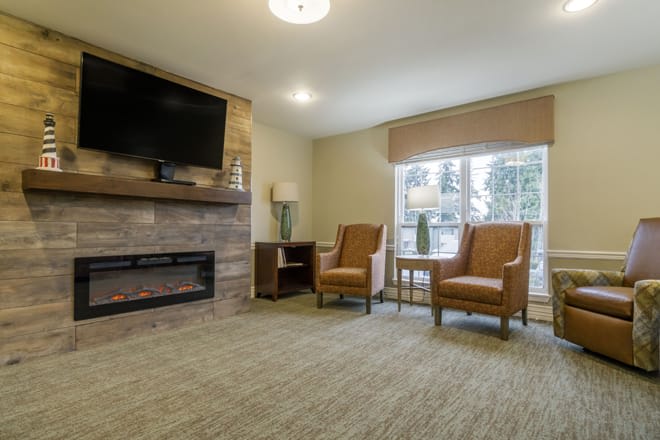 A cozy living room with armchairs, a fireplace, and a large television.