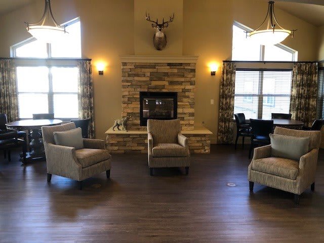 A cozy living room with comfortable armchairs arranged around a fireplace, accented by a deer head on the wall and wood flooring.