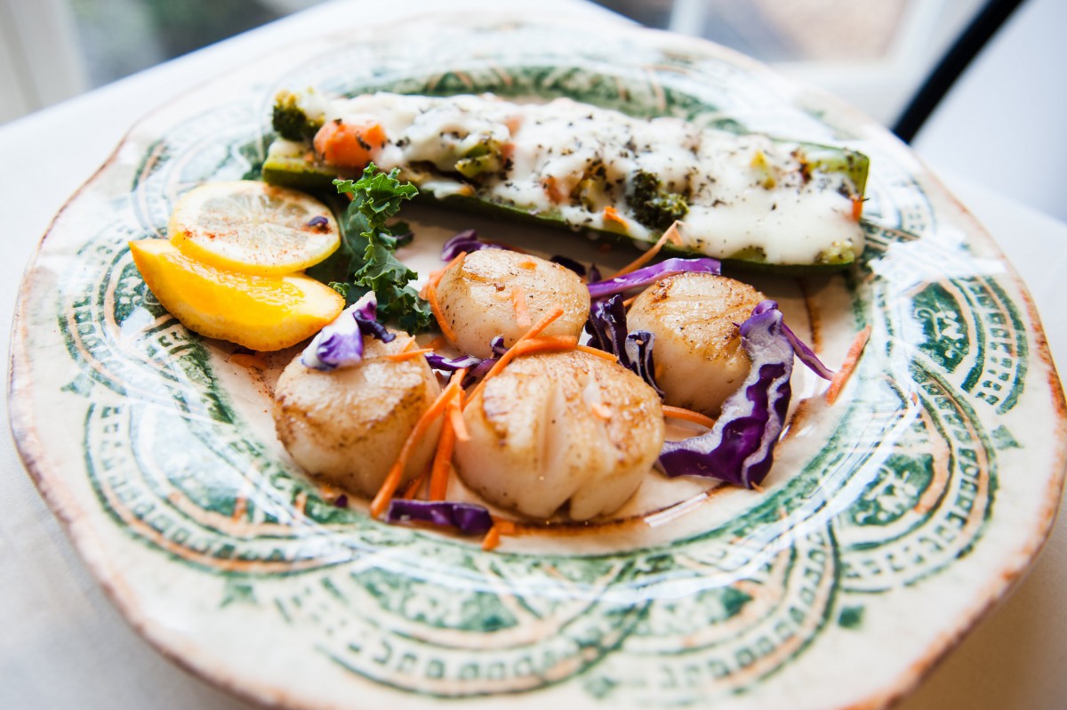 A gourmet plate featuring seared scallops, stuffed zucchini, and lemon garnish.