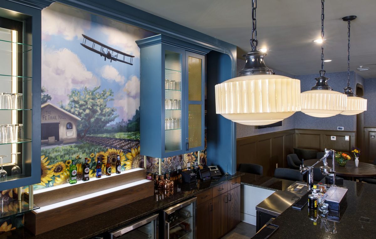 A cozy bar area with a mural featuring an airplane and a scenic backdrop, illuminated by a large decorative light fixture.