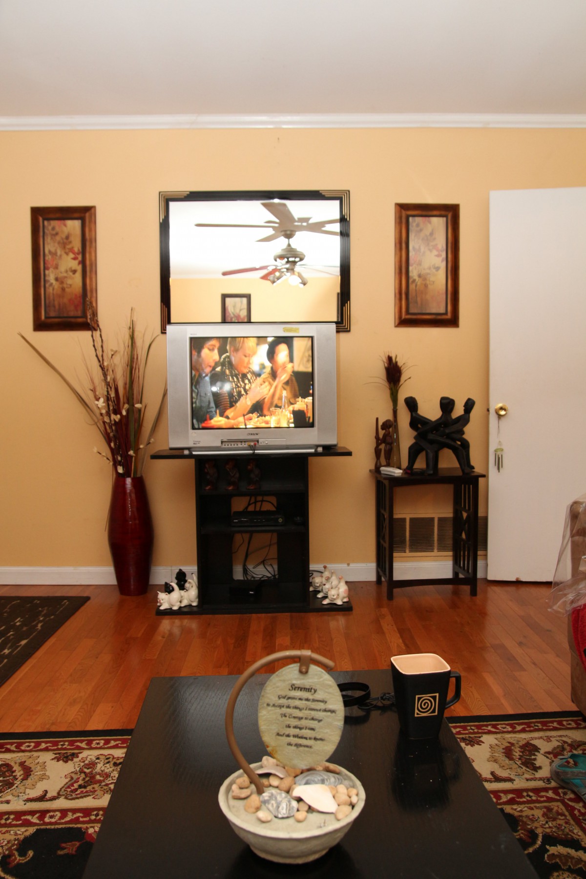 A cozy living room with a television, wooden floors, and decorative elements including framed art and a vase.