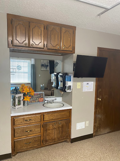 A cozy kitchen corner featuring a sink, wooden cabinets, a mirror, and a television.