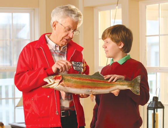 An elderly man and a young boy examining a fish sculpture indoors.