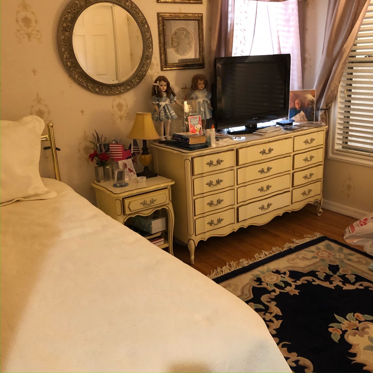 A cozy bedroom with vintage-style furniture featuring a dresser, mirror, and television.