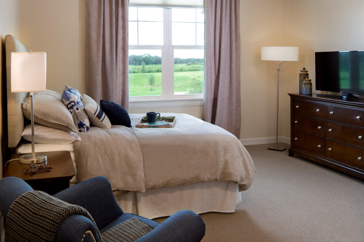 A cozy bedroom with a bed, chair, and window view of the outdoors.