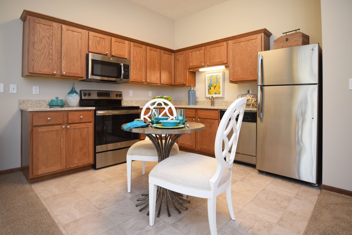A modern kitchen with wooden cabinets, stainless steel appliances, and a small dining area.