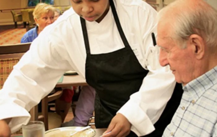 A chef is serving a meal to a diner in a restaurant setting.