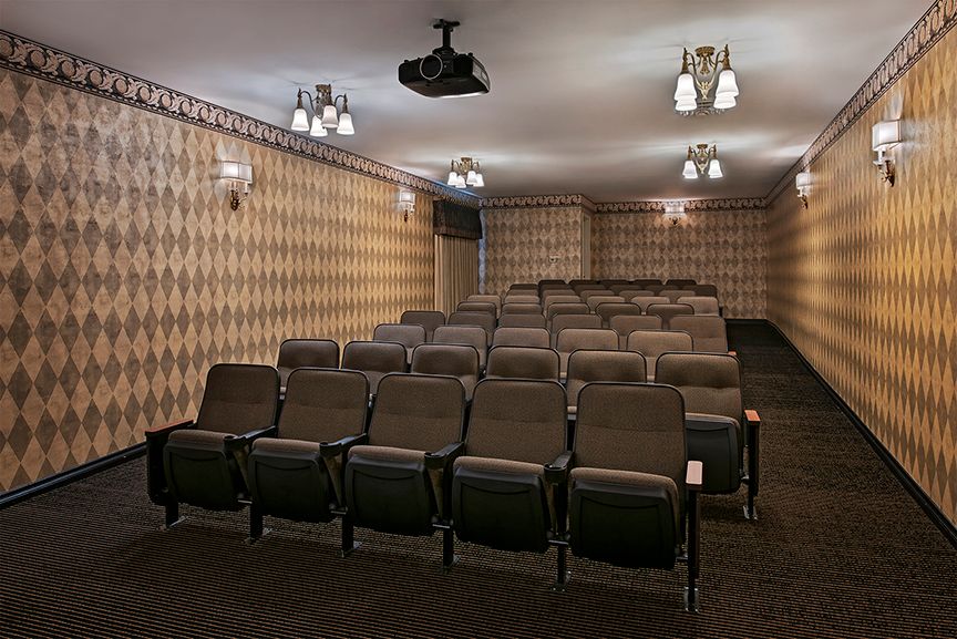 An empty home theater with rows of seating and a ceiling-mounted projector.