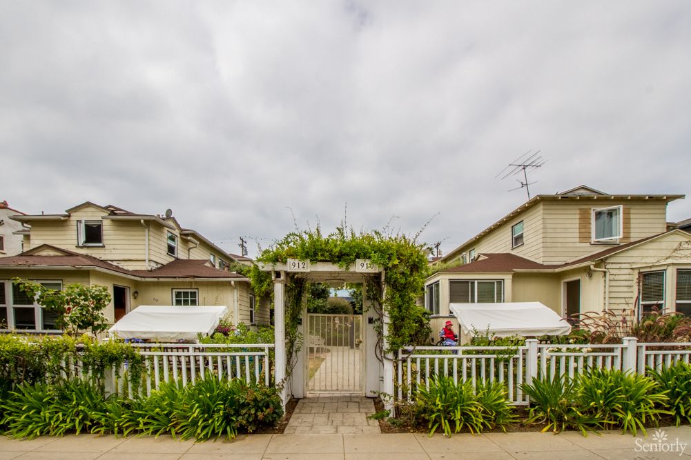 A charming residential area with a gated entrance and lush greenery surrounding twin houses under an overcast sky.