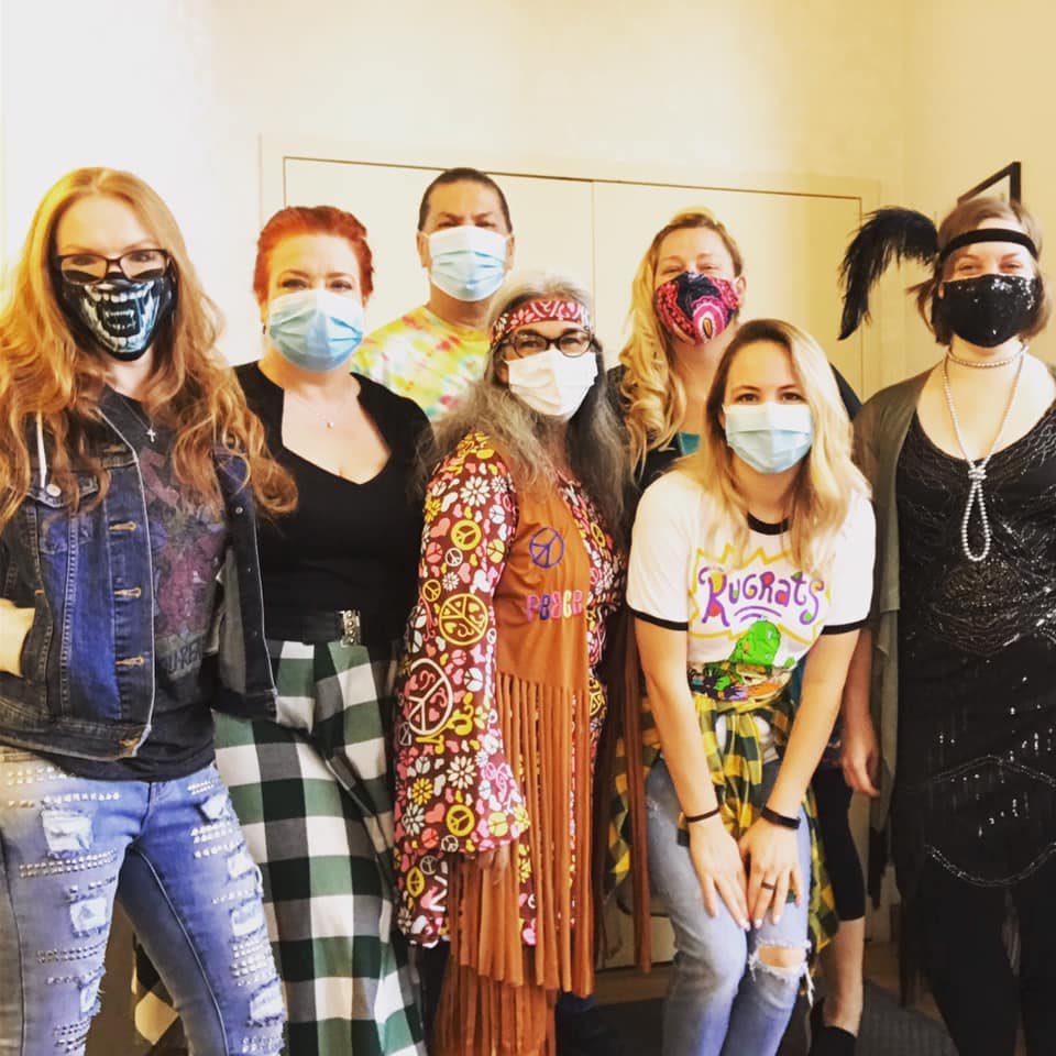 A group of people wearing masks, dressed in a variety of styles, standing indoors.