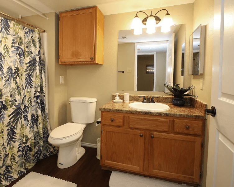 A well-organized bathroom with wooden cabinetry, a sink, and a shower with a floral curtain.