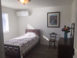 A minimalist bedroom with a single bed, a chair, and a framed painting on the wall.