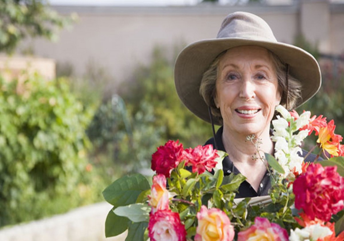 A senior woman smiling while holding a bouquet of flowers in a garden.