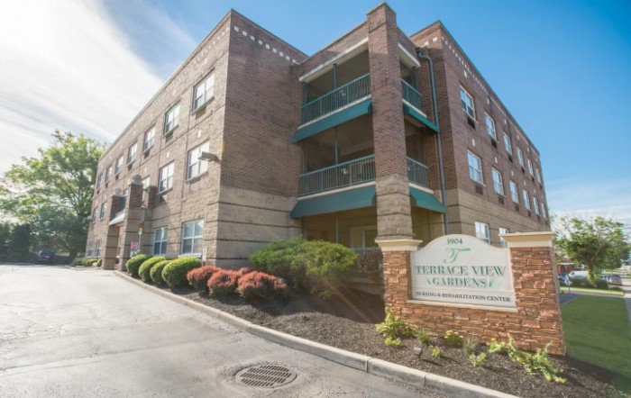 A brick apartment building with well-maintained landscaping and a sign at the entrance.
